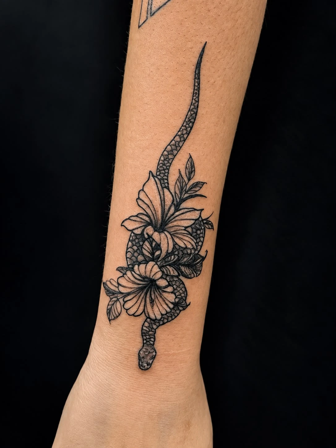 Tatuagem fina de cobra com flores no antebraço